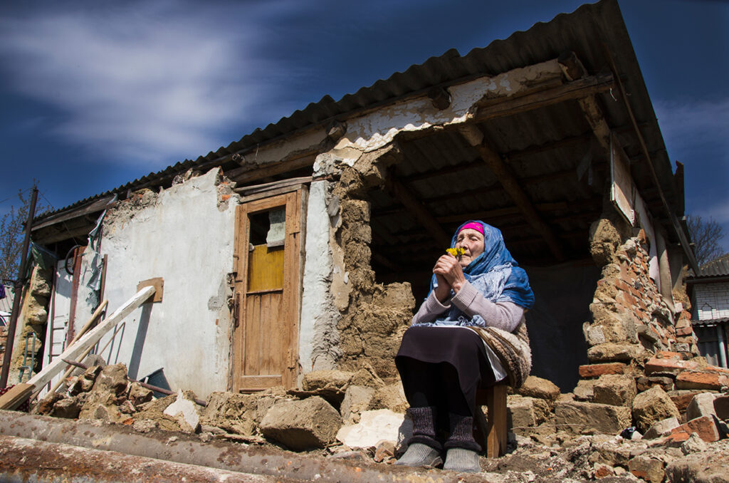 A woman next to a house destroyed by the war. War in Ukraine. Ukrainian refugees. Grandmother in the ruins of her house destroyed by the war. Peace concept